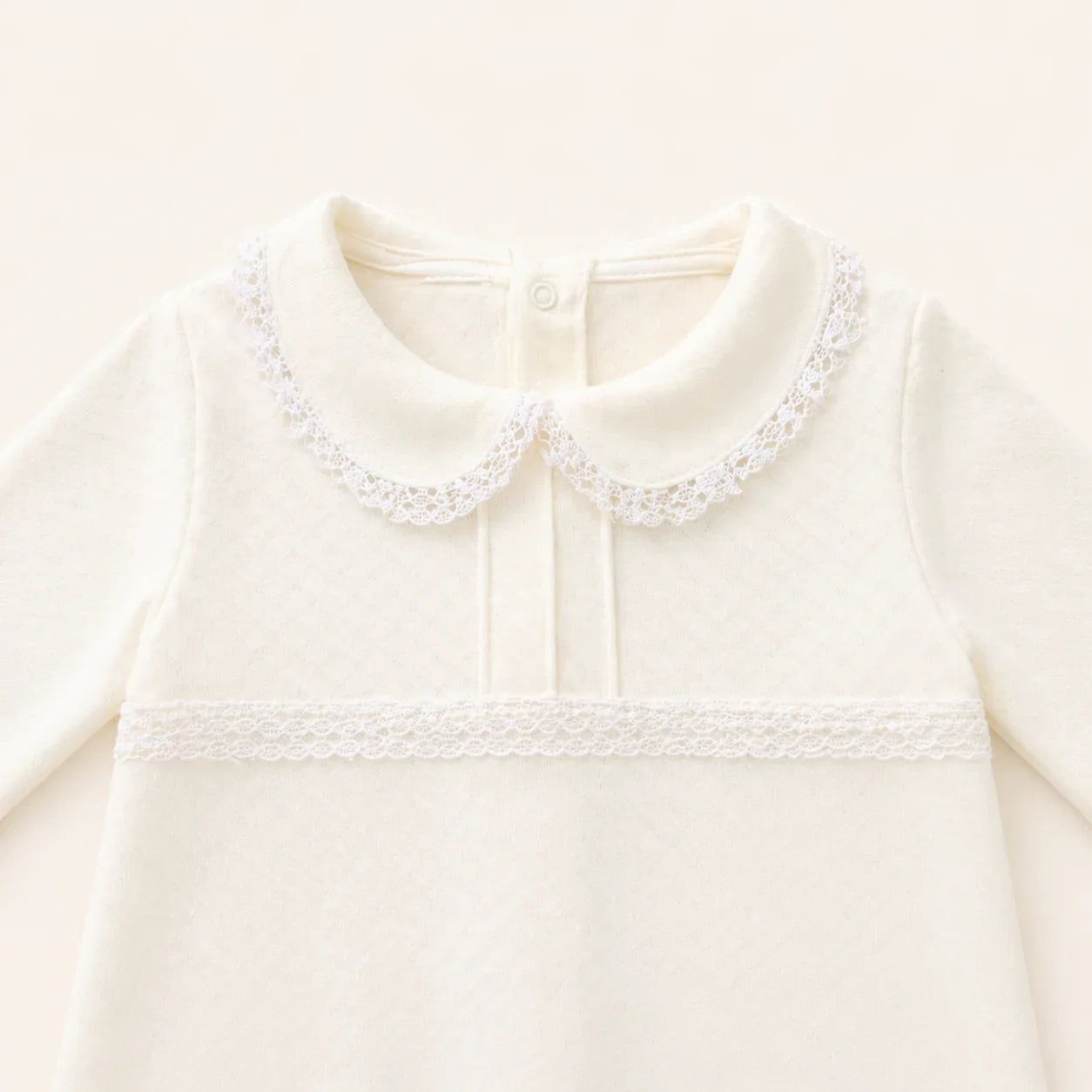 Babygrow bege de malha para bebé, gola Peter Pan e detalhes em renda, manga comprida.