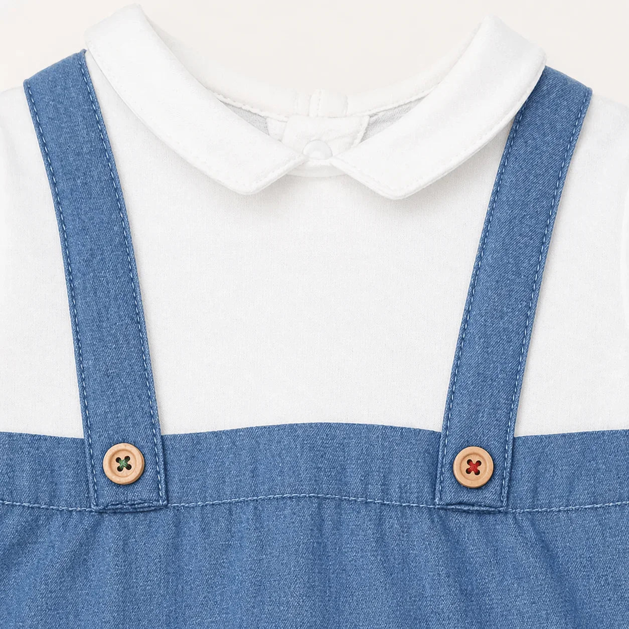 Detalhe de babygrow de algodão azul denim com alças e botões de madeira para bebé.