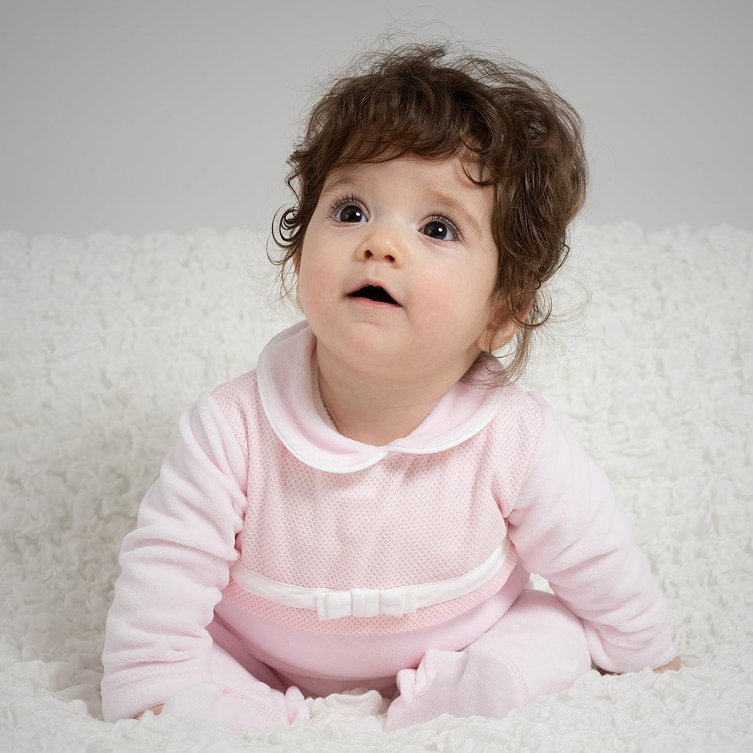 bebê sentado com babygrow rosa de manga comprida e laço, sobre manta branca, roupa confortável para recém-nascido