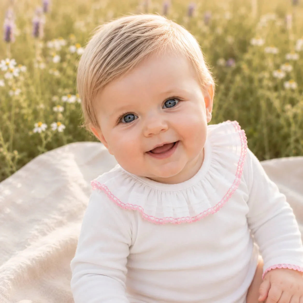 Bebê sorridente com roupa branca e detalhes rosa em campo de flores