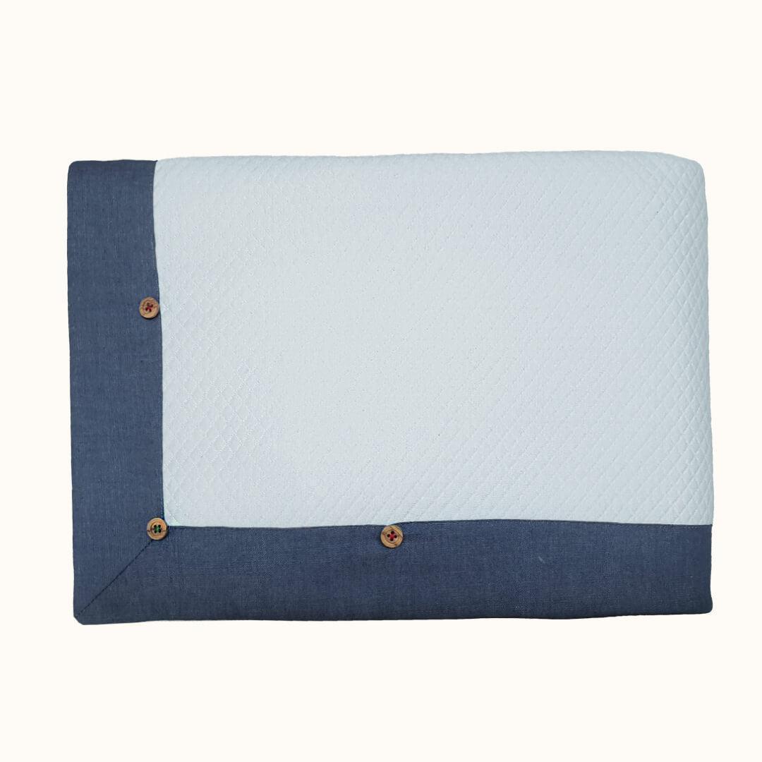Manta de bebê azul e branca com barra em jeans e botões decorativos, enxoval delicado.