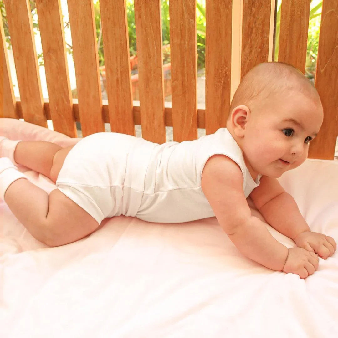 Bebê veste body branco sem mangas em berço de madeira, roupa confortável para recém-nascidos.