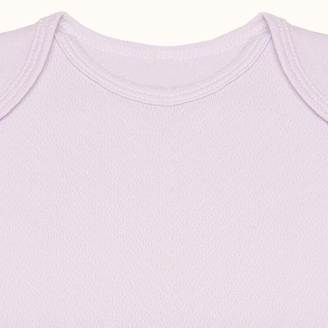 Detalhe do ombro e gola envelope de body de bebé em algodão rosa claro, manga curta.