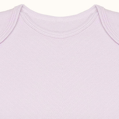 Detalhe do ombro e gola envelope de body de bebé em algodão rosa claro, manga curta.