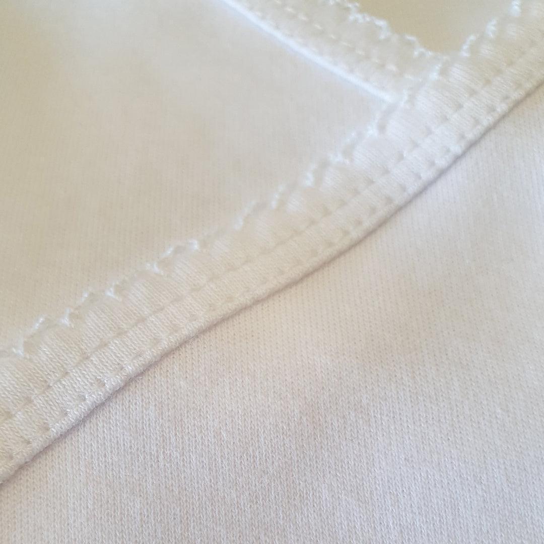 Detalhe de costura em tecido branco de roupa de bebê, foco em qualidade e conforto.