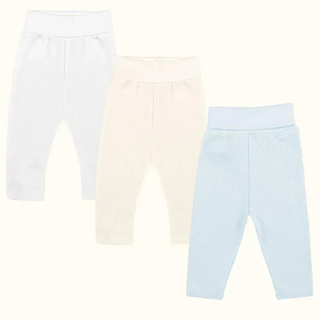 Três calças de bebé sem pé em algodão, cores branco, bege e azul claro, fundo neutro.
