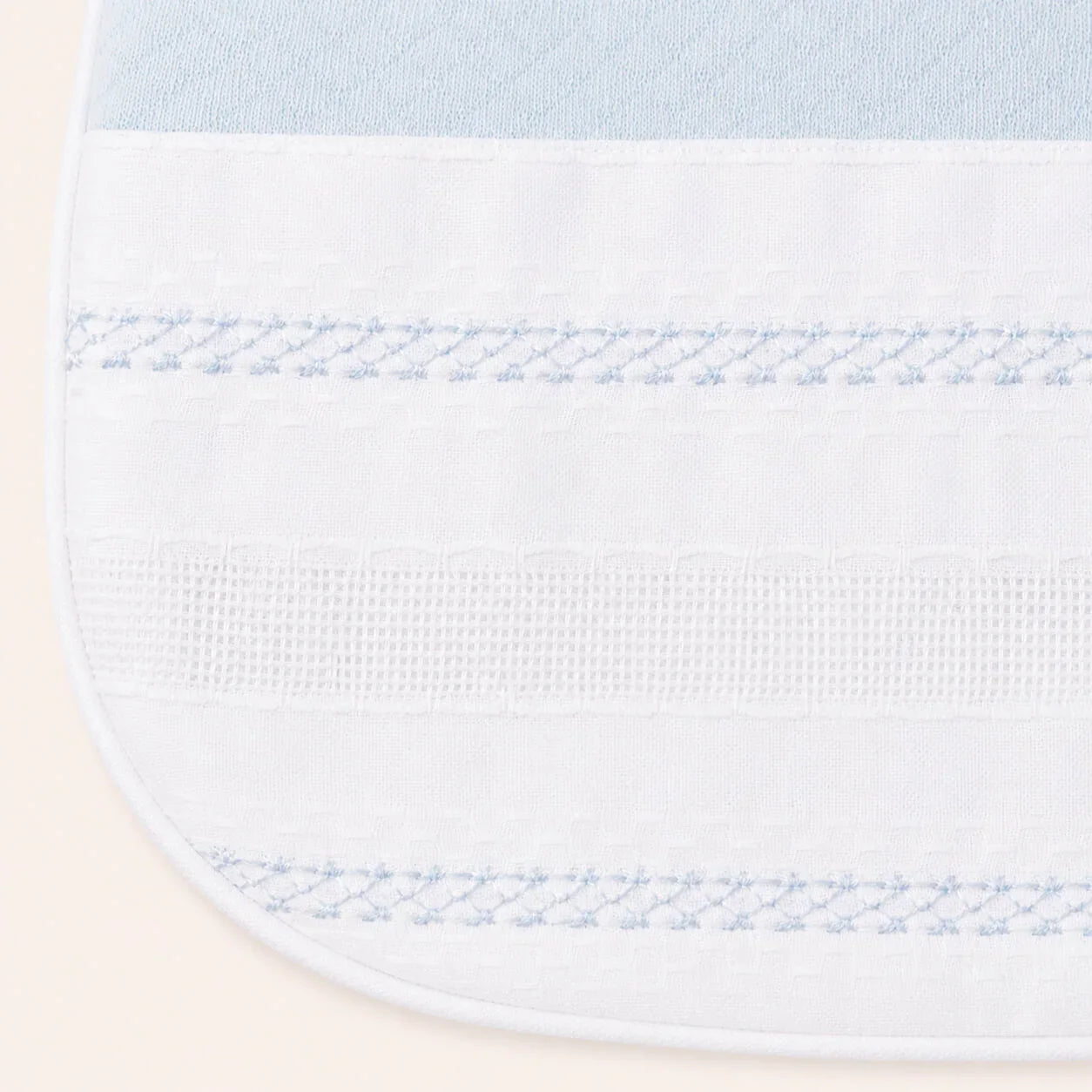 Babete de bebé branco com detalhes azul claro e bordado delicado, tecido suave.
