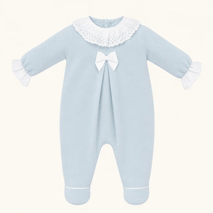 Babygrow azul de malha para bebê com gola e punhos de renda branca e laço decorativo.