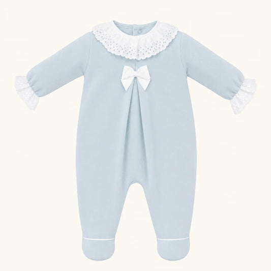 Babygrow azul de malha para bebê com gola e punhos de renda branca e laço decorativo.