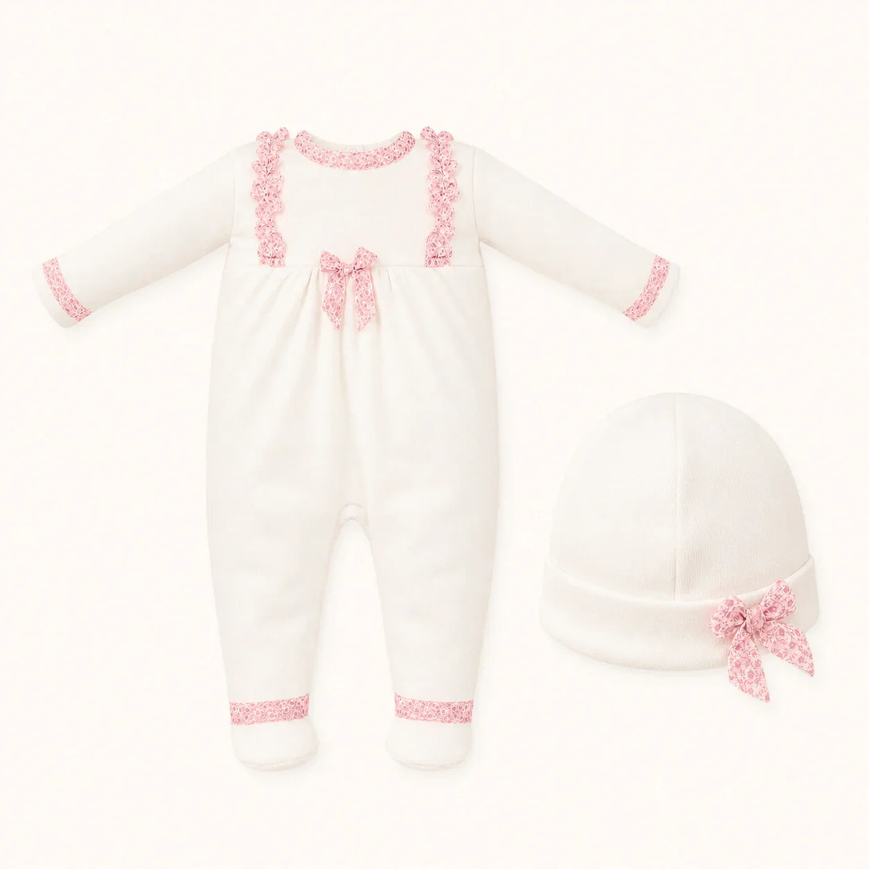 Conjunto de babygrow branco para bebé com detalhes rendados rosa e gorro combinando.