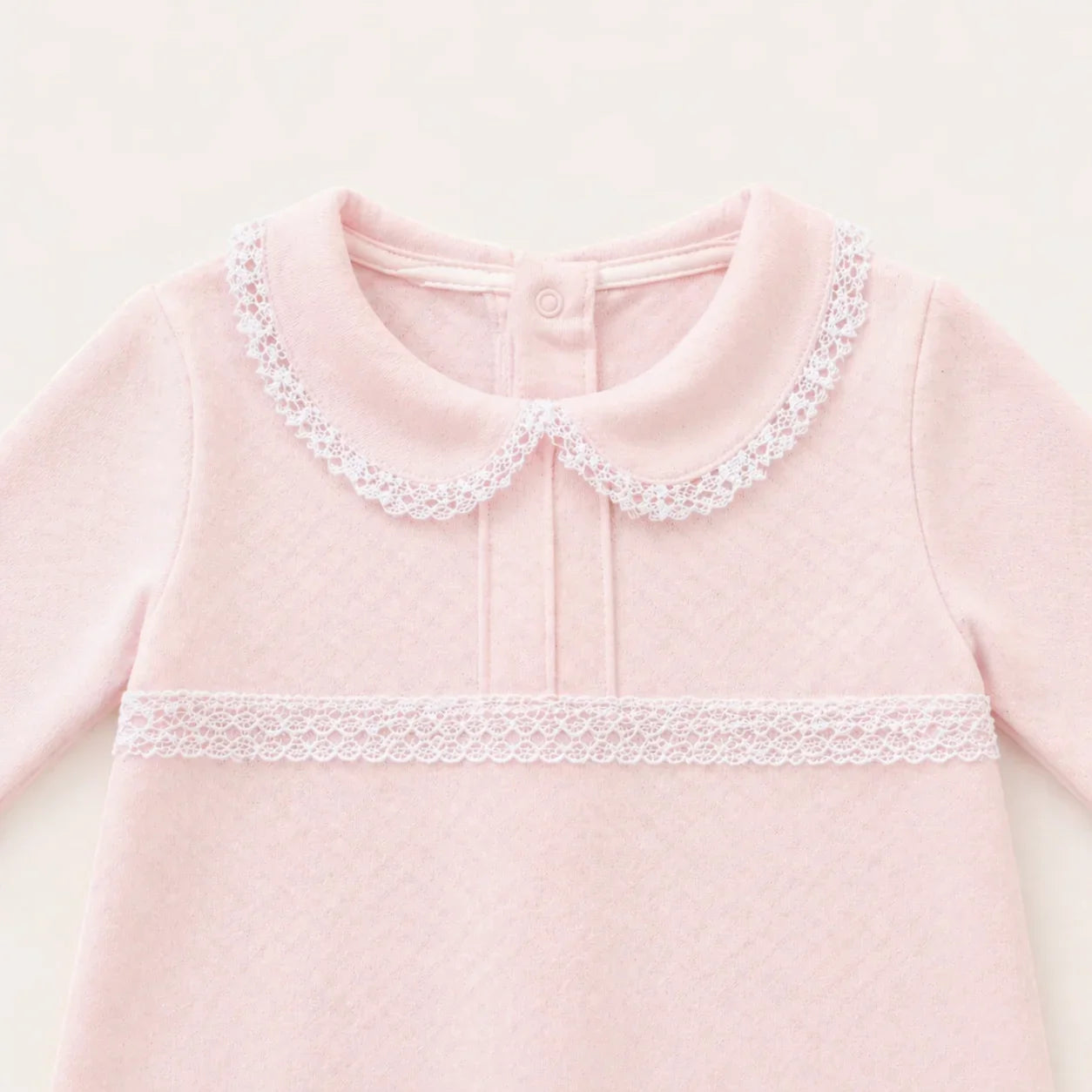 Babygrow rosa para bebé em algodão suave, gola peter pan e detalhe de renda branca.