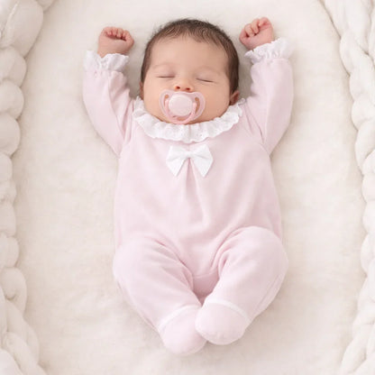 Bebê dormindo em ninho, vestindo babygrow rosa com laço e gola de babados delicada.