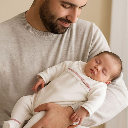 Bebé dormindo vestido com babygrow bege com detalhes rosa velho, colo do pai, roupa confortável para recém-nascido.