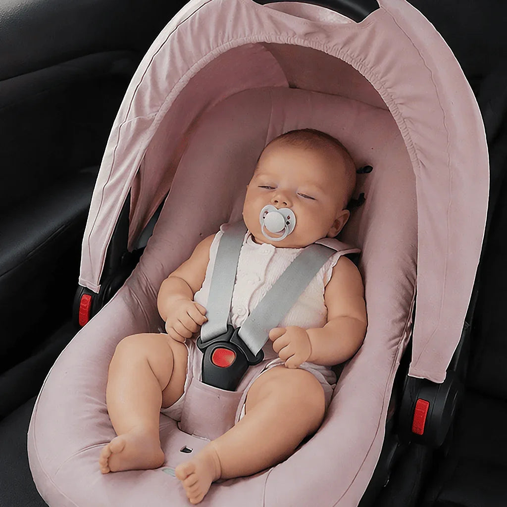Bebê dormindo em cadeirinha rosa de carro com chupeta e cinto de segurança