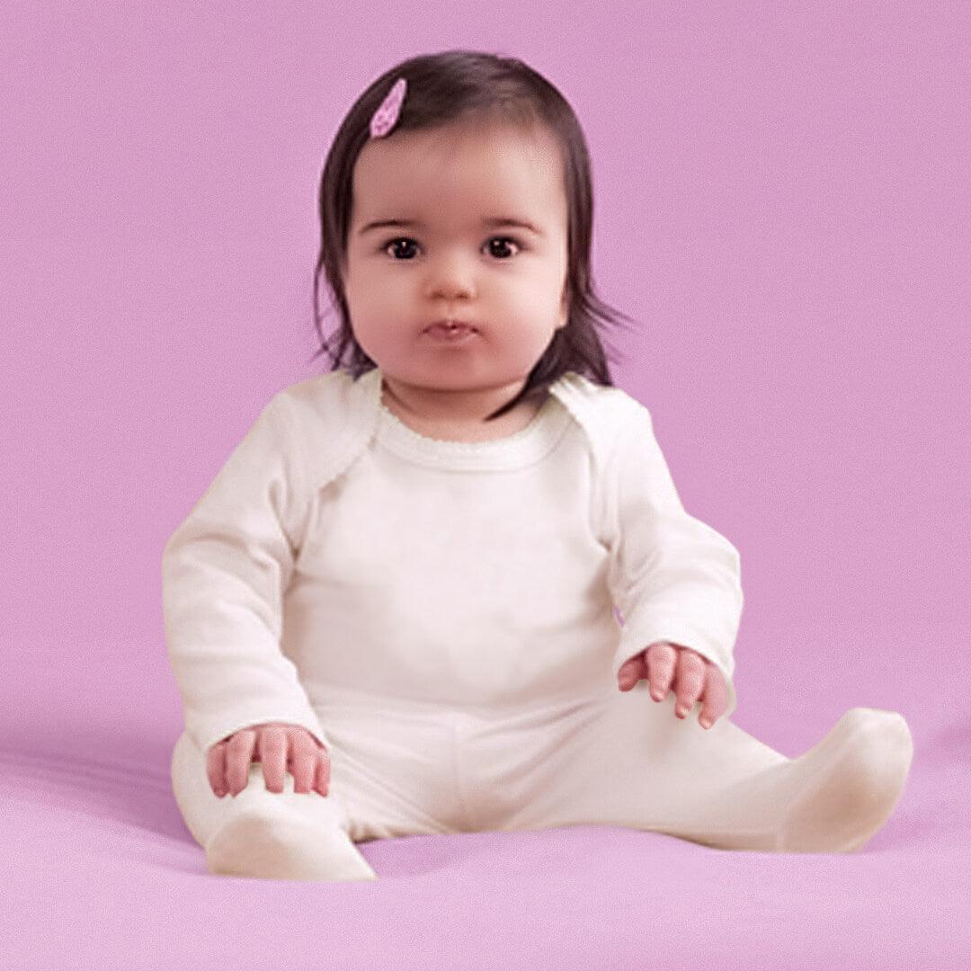 Bebé sentada usando body de manga comprida bege, com fundo rosa, roupa confortável para recém-nascido.