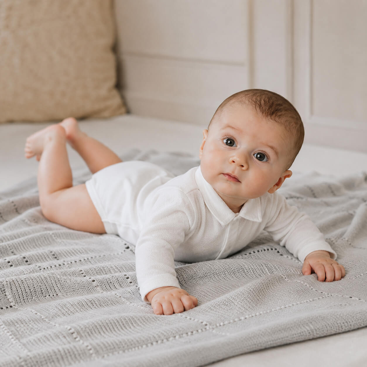 Bebé deitado numa manta, vestido com body de gola camisa, malha algodão branco, super macia e com tratamento Anti-Pilling e anti-encolhimento