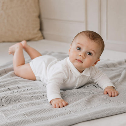 Bebé deitado numa manta, vestido com body de gola camisa, malha algodão branco, super macia e com tratamento Anti-Pilling e anti-encolhimento