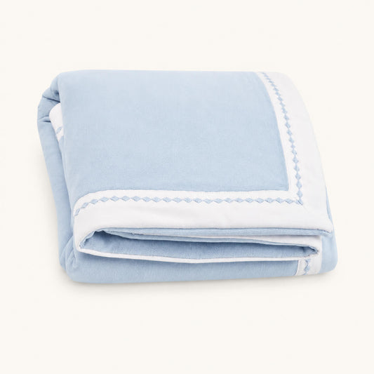 Manta para bebé dobrada em azul com barras em branco com pormenor losangos bordados em azul