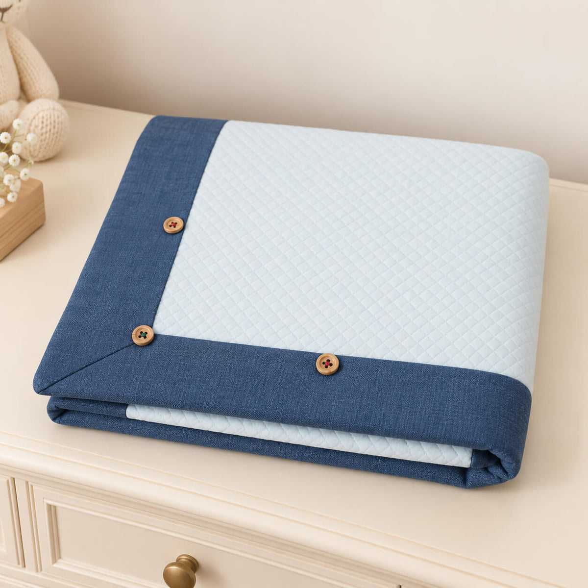 Manta essencial para bebé em malha losango de algodão azul claro e com barras azuis denim, dobrada sobre uma cómoda 