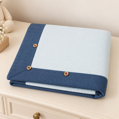 Manta essencial para bebé em malha losango de algodão azul claro e com barras azuis denim, dobrada sobre uma cómoda 