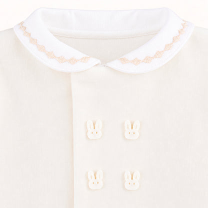 Detalhe de babygrow bege para bebê com gola bordada e botões decorativos de coelhinho.
