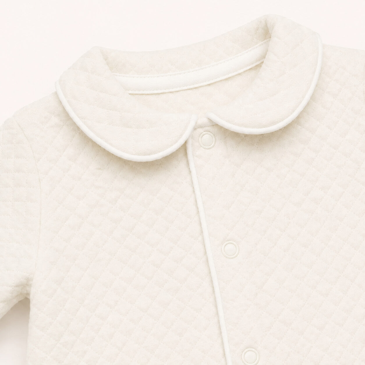 Pormenor da gola redonda com vivo branco do babygrow prestige em bege. Tudo muito delicado a pensar na pele sensível do bebé 