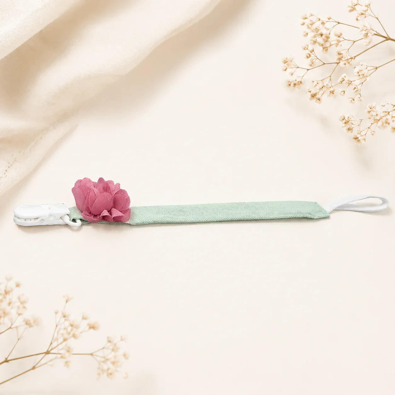 Suporte de chupeta verde com flor rosa decorativa para bebê, em fundo neutro