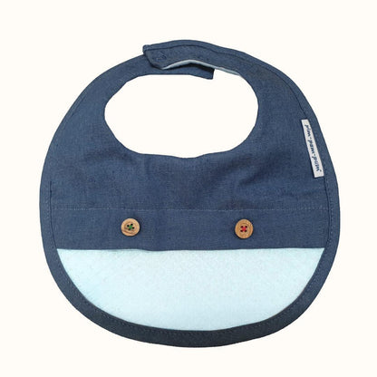Babete impermeável azul denim com botões decorativos para bebé, fundo claro.
