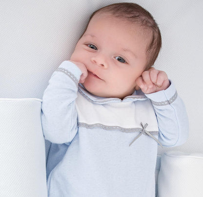 Bebê deitado usando babygrow azul com detalhe de laço cinza, roupa confortável para recém-nascido