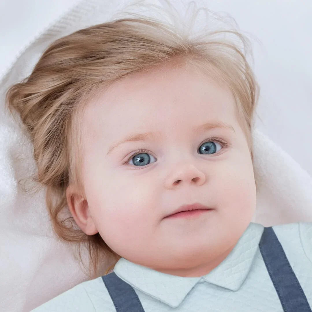 Bebé de olhos azuis com babygrow azul claro sem pés, deitado em manta branca