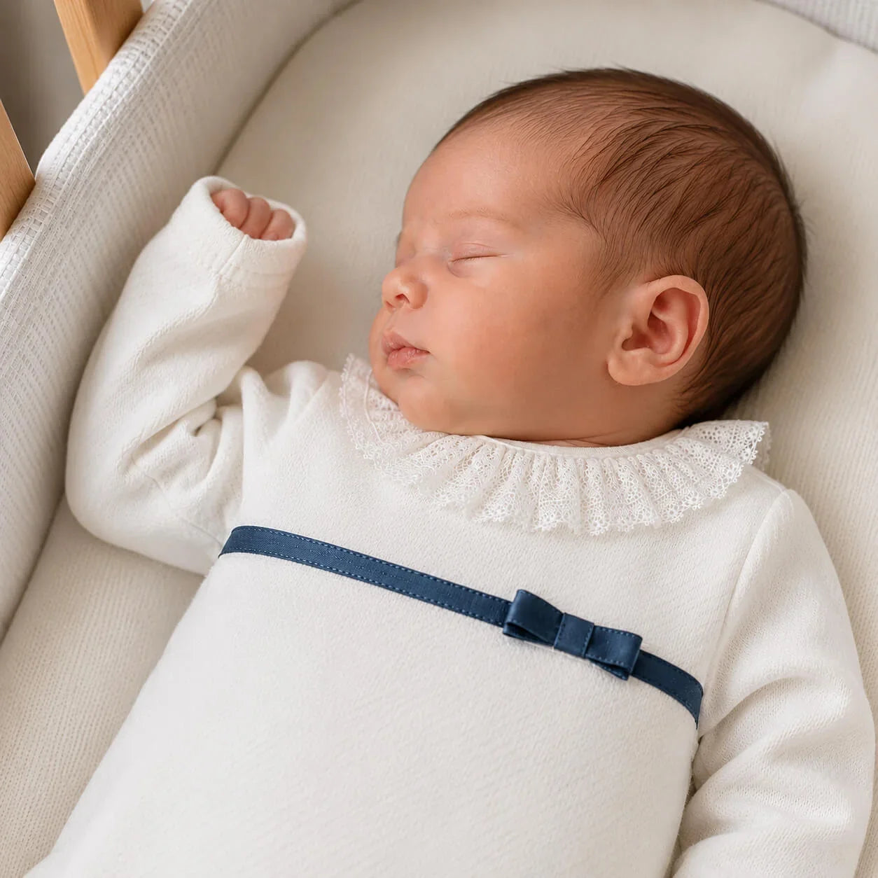 bebé dormindo em roupa bege com babado e laço azul, confortável e delicada para recém-nascidos.