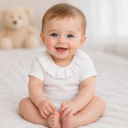 Bebe menino sorridente com body classic branco com gola em bordado inglês, manga curta, tudo em algodão