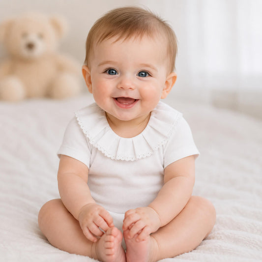 Bebe menino sorridente com body classic branco com gola em bordado inglês, manga curta, tudo em algodão