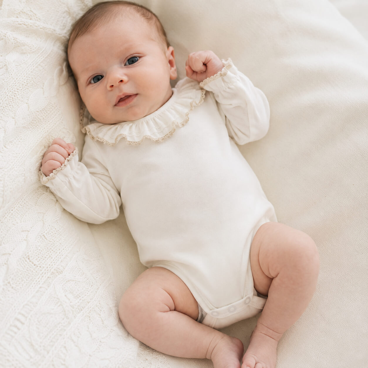 Bebé vestido com um body com gola folho e renda bege em malha algodão bege, sem etiquetas irritantes no decote e abrir de cima a baixo para facilitar a muda da roupa