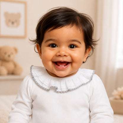 Bebe sorridente com body branco com renda cinza, manga comprida, tudo em algodão