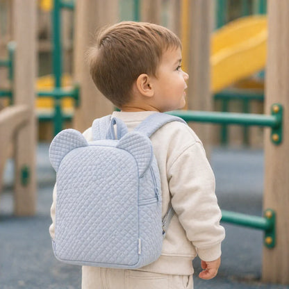 bebé com mochila azul acolchoada com orelhas em parque infantil, roupa confortável de bebé.