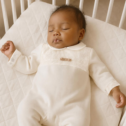 Bebê dormindo em roupa branca com detalhe de laço, confortável e suave para recém-nascidos