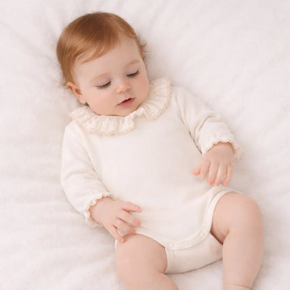 Bebé deitado com body branco de manga longa e gola babado, roupa confortável para recém-nascido.