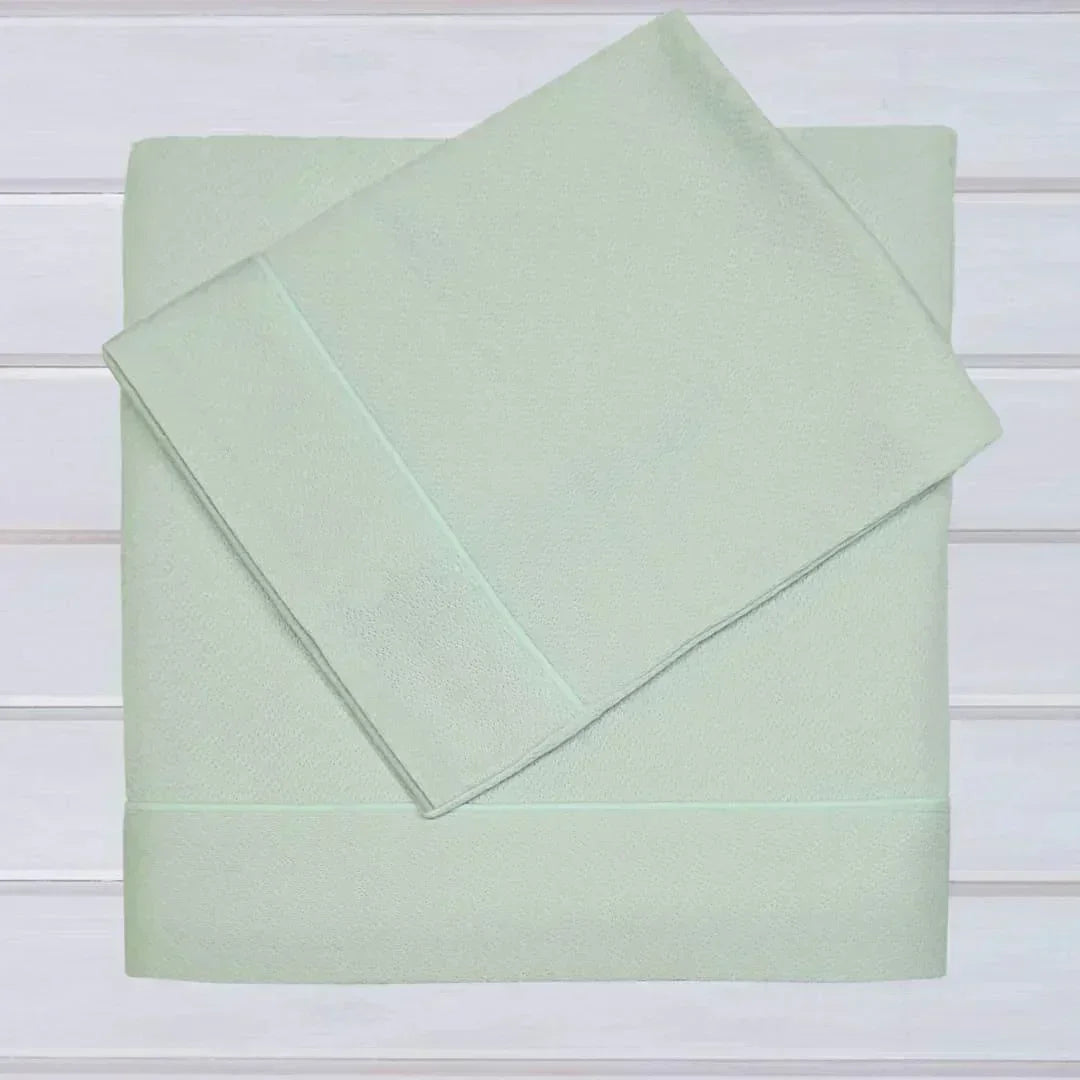 Conjunto de lençóis de malha em algodão para berço, cor verde clara, dobrados sobre fundo branco.