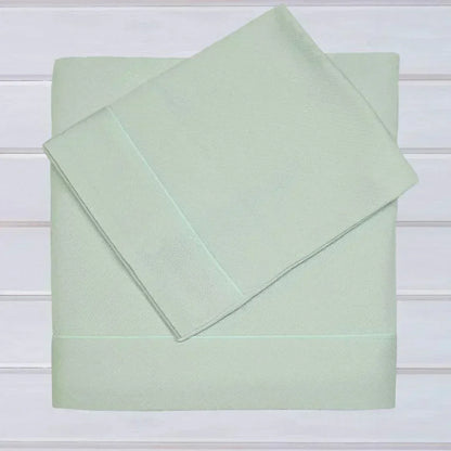 Conjunto de lençóis de malha em algodão para berço, cor verde clara, dobrados sobre fundo branco.