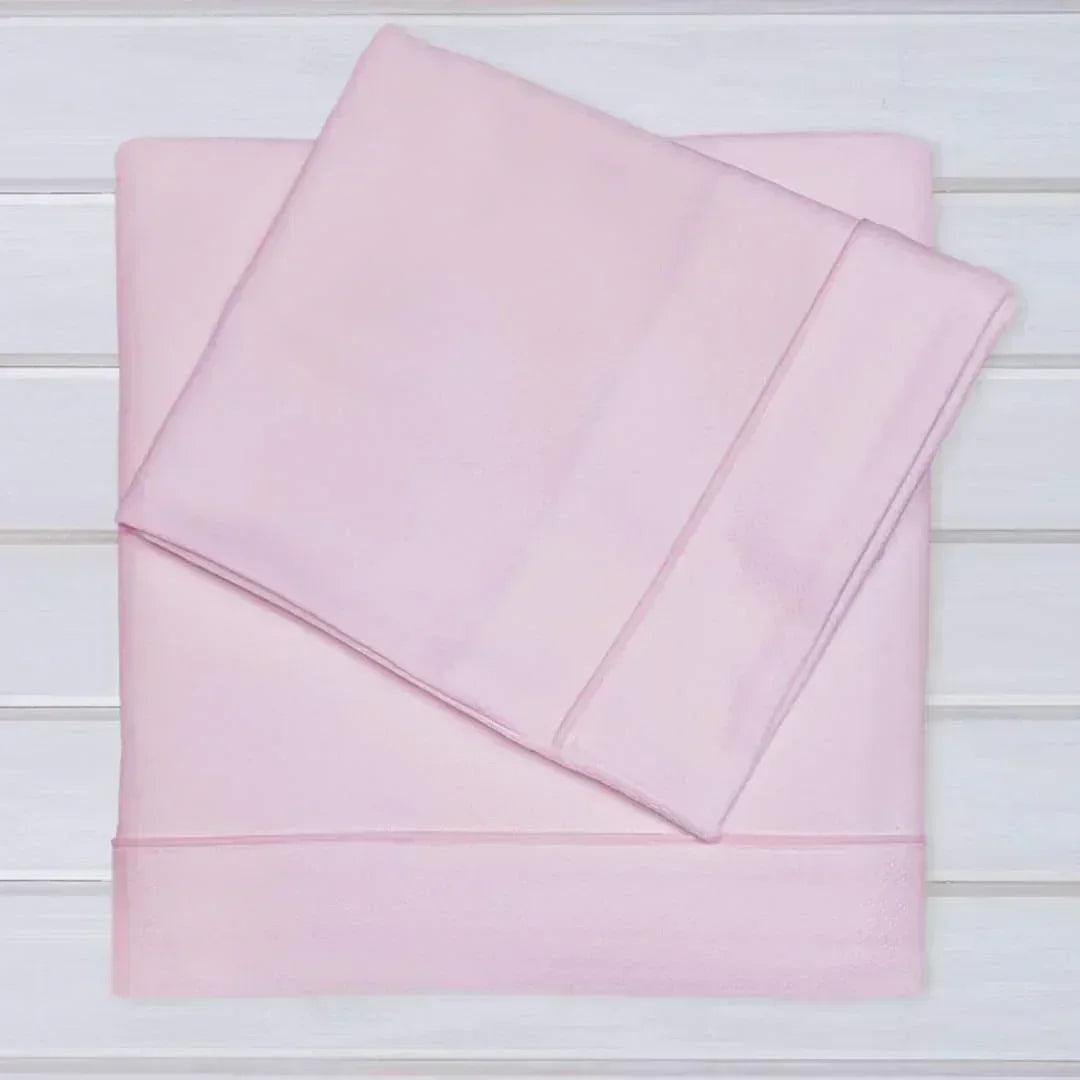Conjunto de lençóis rosa claro em algodão para bebé, sobre superfície branca, enxoval infantil.