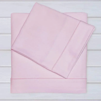 Conjunto de lençóis rosa claro em algodão para bebé, sobre superfície branca, enxoval infantil.