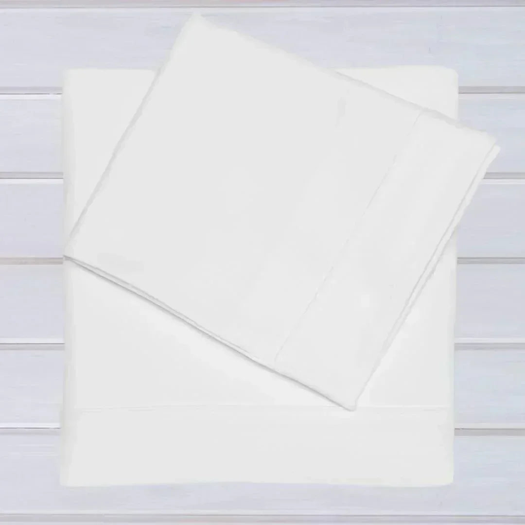 Conjunto de lençóis brancos para berço em algodão, ideal para bebé, sobre fundo de madeira clara.