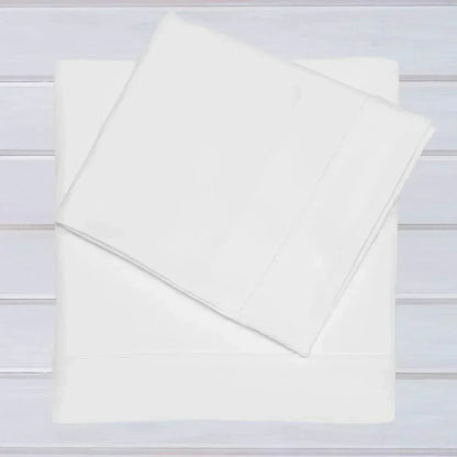 Conjunto de lençóis brancos para berço em algodão, ideal para bebé, sobre fundo de madeira clara.