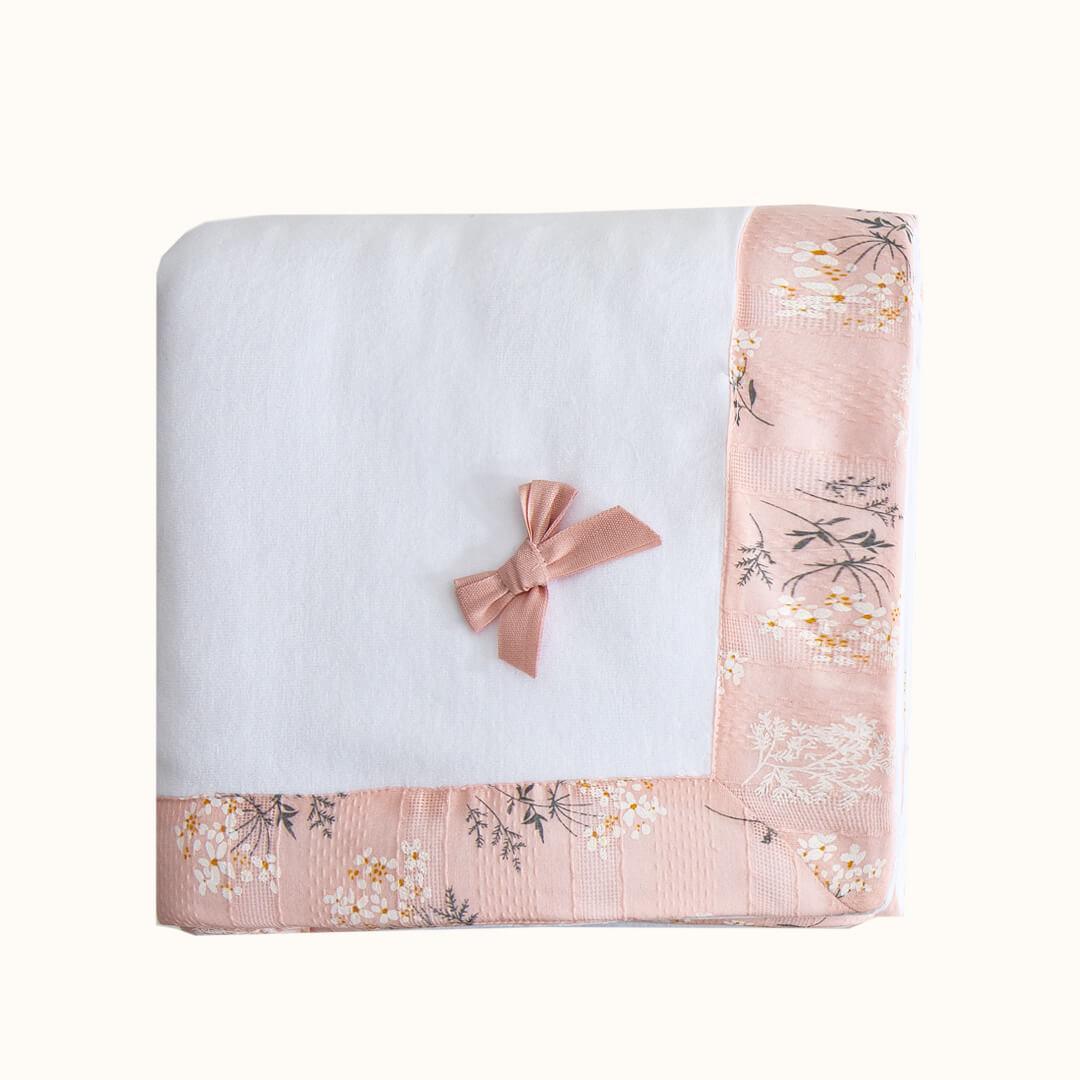 Manta de bebê branca com laço e faixa floral rosa, ideal para enxoval de recém-nascido.