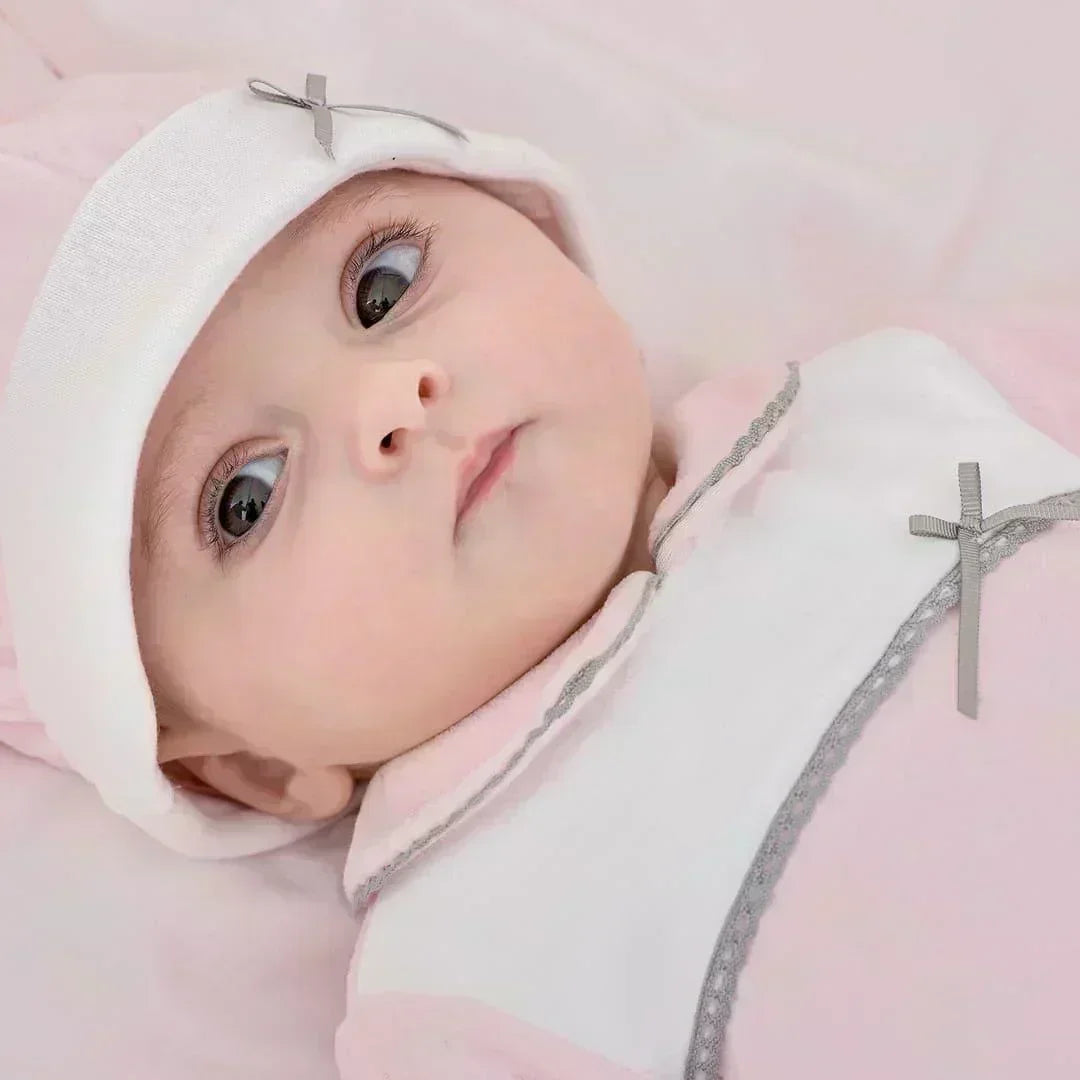 bebê vestindo conjunto primeira roupa rosa e branco com laços cinza, deitado em fundo claro
