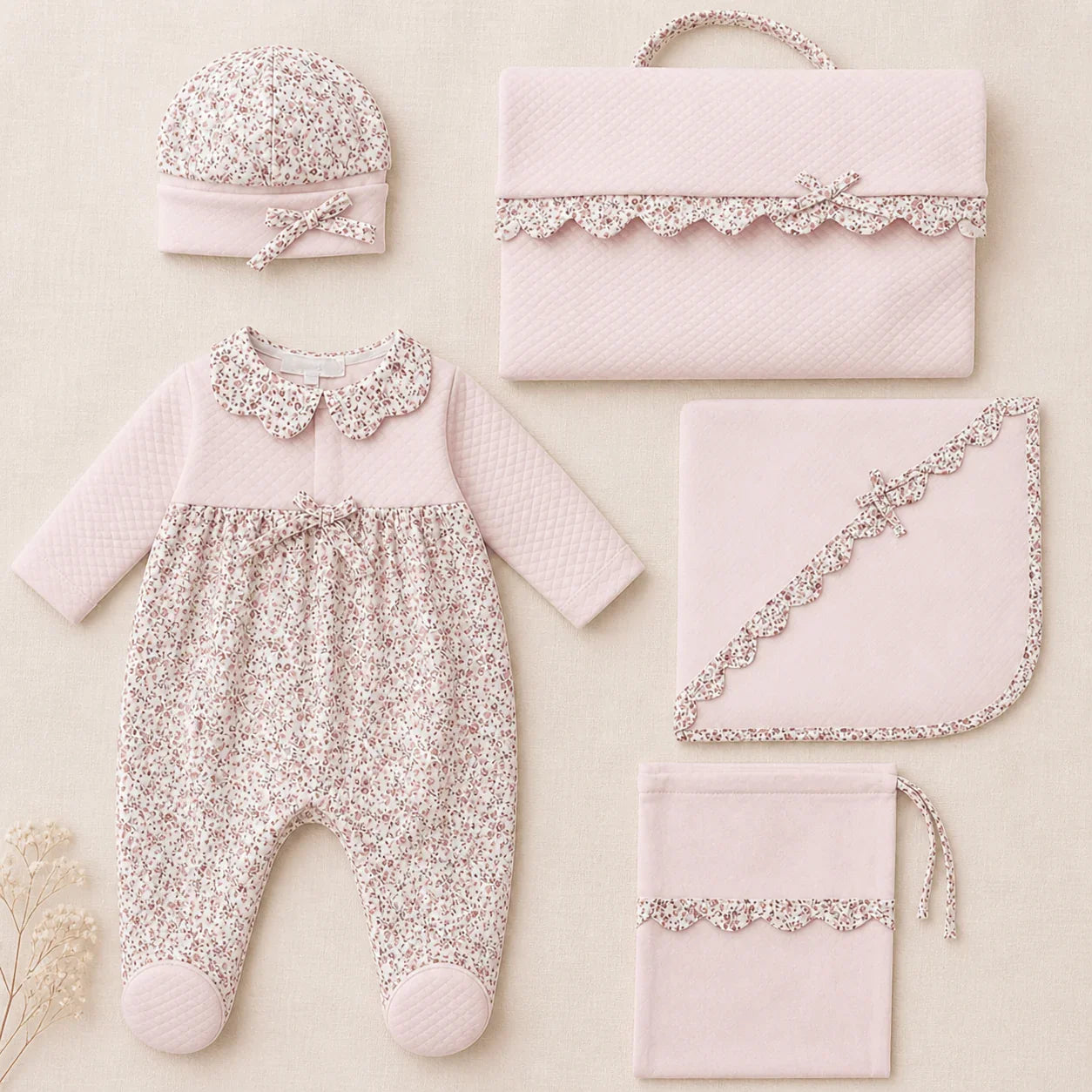 Conjunto enxoval de recém-nascido rosa claro com estampa floral, incluindo macacão, touca, manta e bolsa.