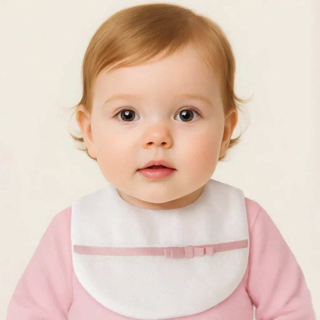 bebê usando babador branco com laço rosa, roupa rosa, fundo claro, moda infantil confortável