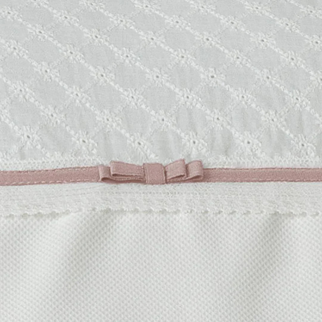 Detalhe de edredom para bebé branco com laço rosa e textura delicada, enxoval infantil