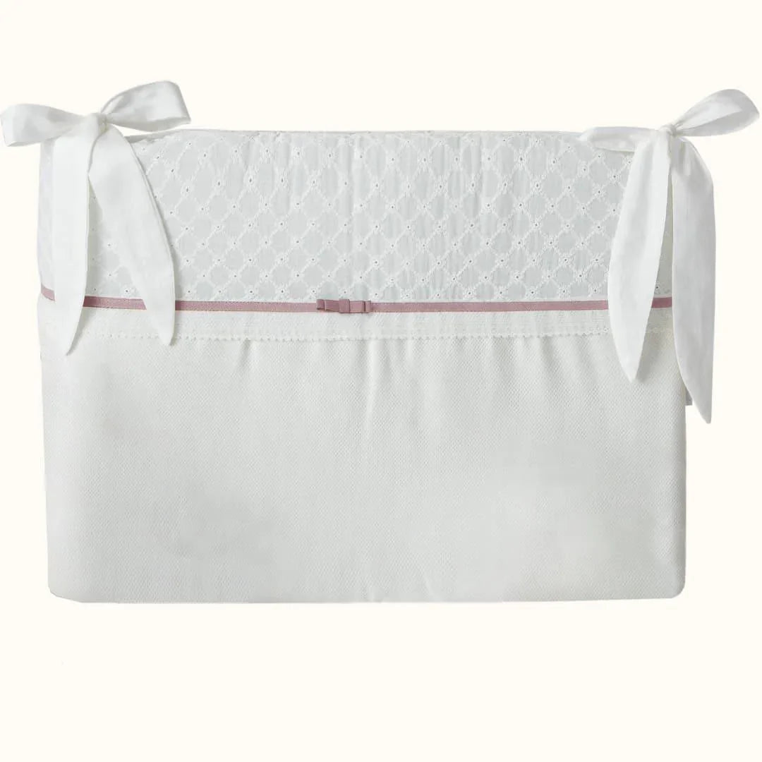Protetor de berço bege e branco com laços e detalhe rosa, delicado para enxoval de bebê.